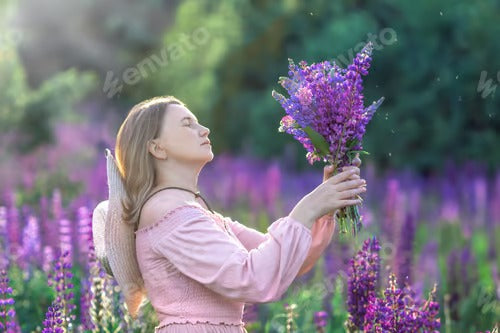 A girl with blondy hair in the summer in a field of blooming purple lupine flowers with a bouquet