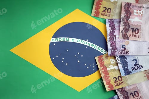 Brazilian money bills on top of the national flag of Federative Republic of Brazil