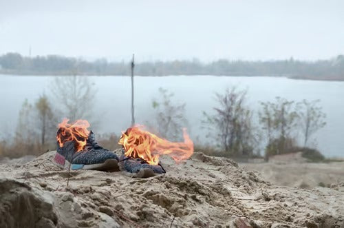 Burning sports sneakers or gym shoes on fire stand on sandy beach coast.