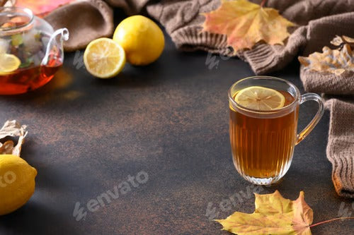 Warming black tea with lemon in cozy lifestyle with fall leaves and cozy scarf.